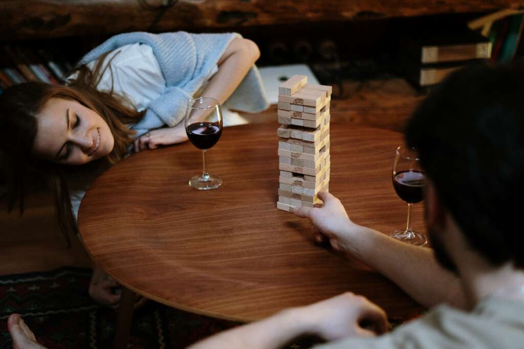 2 people playing Jenga with 2 glasses of red wine.