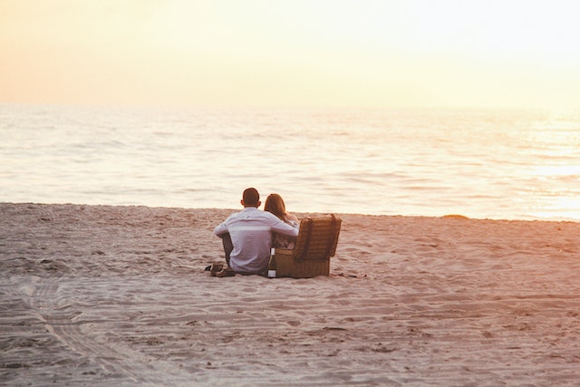 A couple sitting on the beach by a sunset