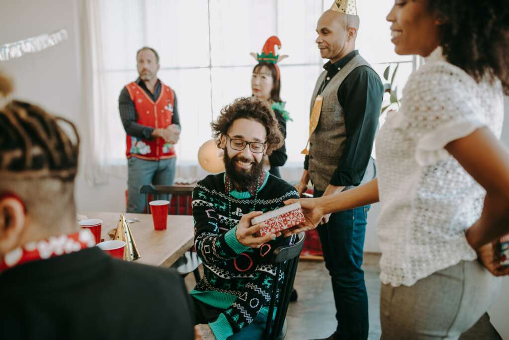 A room of people celebrating a holiday party. A person receiving a gift from another person.