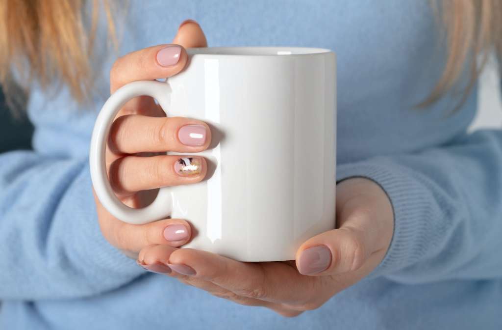 Female hands hold mock up white empty mug, cup for your design and logo closeup