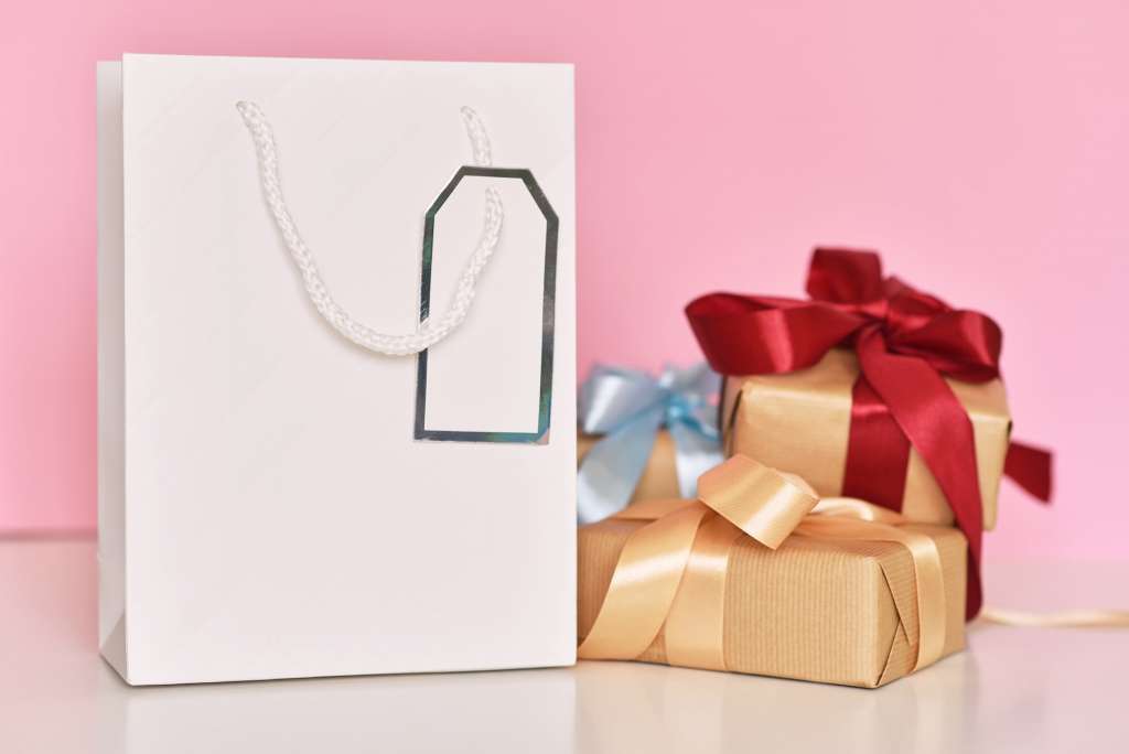 Gift box with ribbon and paper shopping bag on a pink background