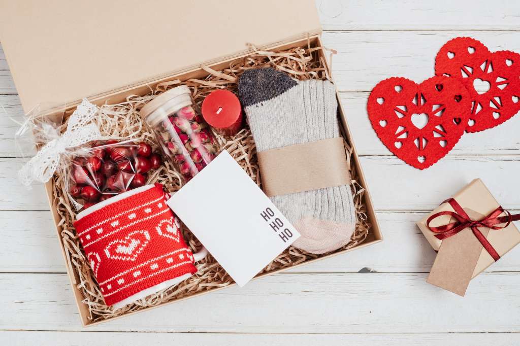 Preparing care package, seasonal gift box with mug, candle, woolen socks and christmas ornament