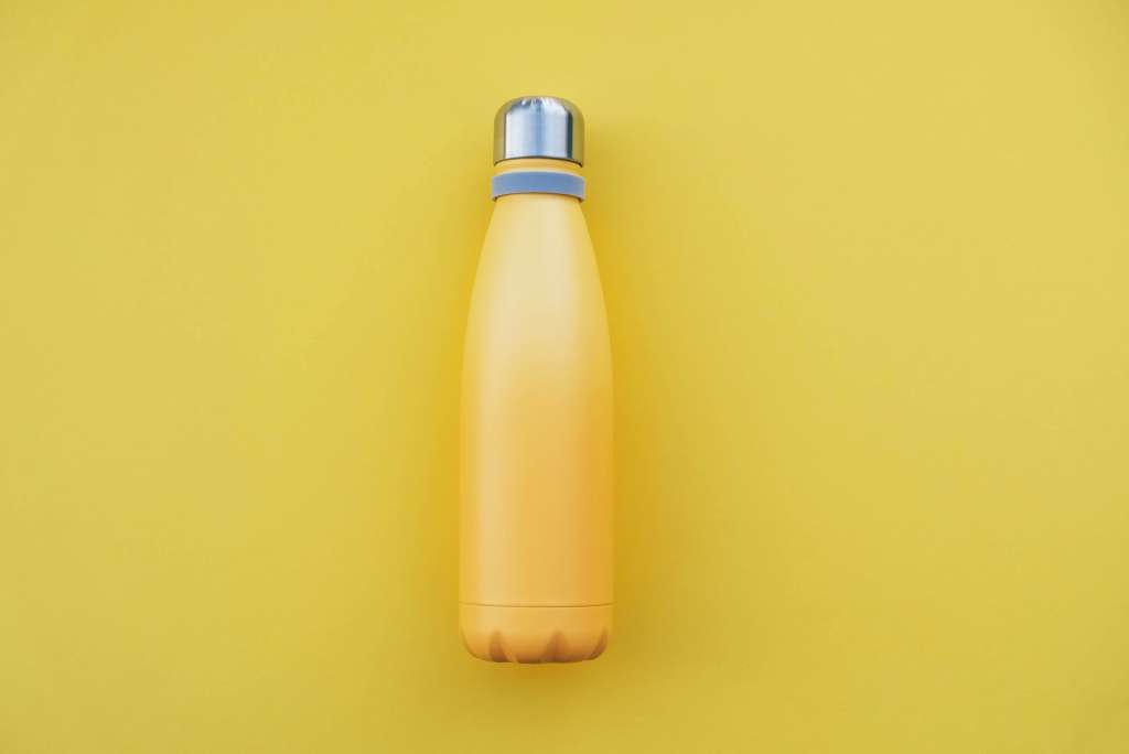 Reusable eco friendly stainless steel water bottle on yellow background.