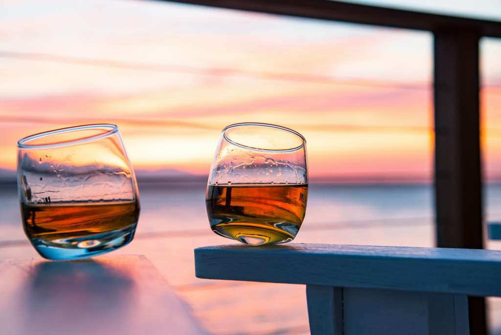Tumbler whiskey drink glasses on sea view deck chairs at sunset