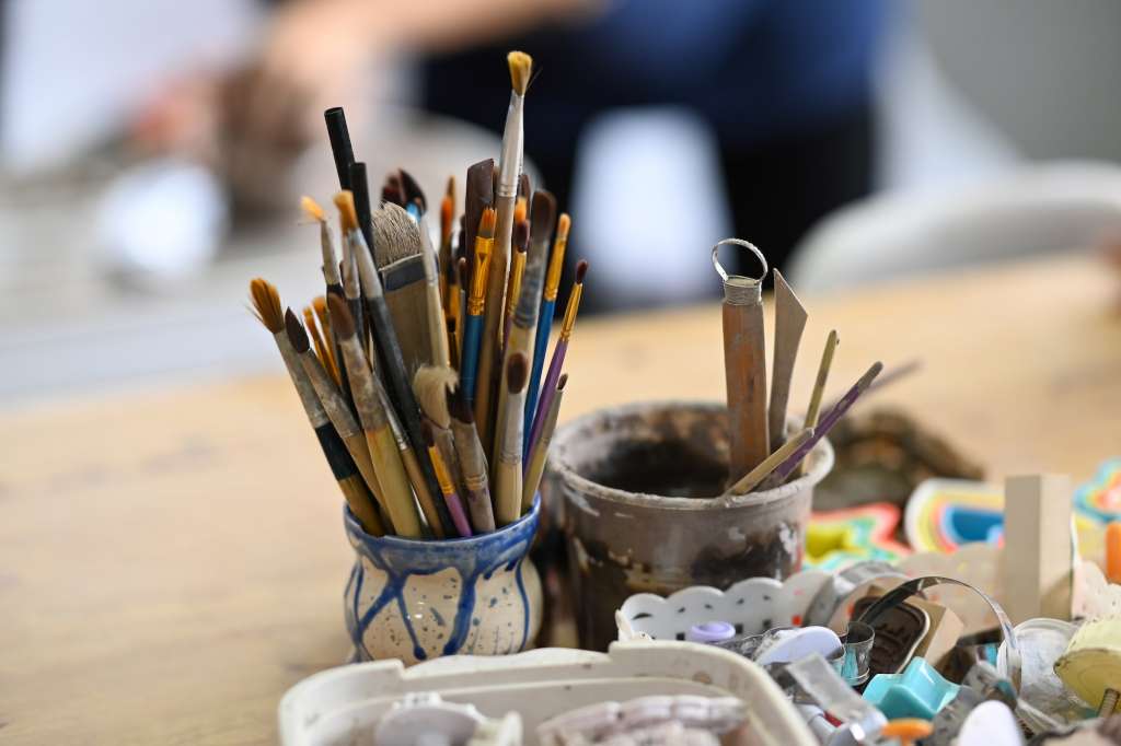 Ceramics making equipment with paint brushes, pottery shaping tools on wooden table.