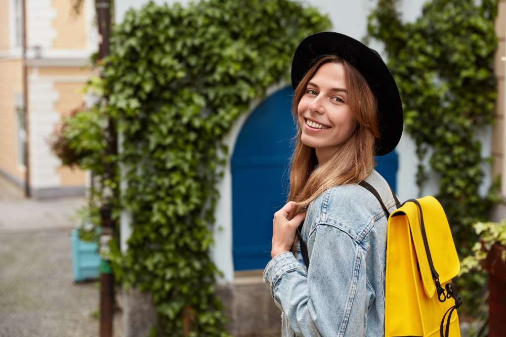 young female employee with yellow bagpack, wears black hat and denim jacket