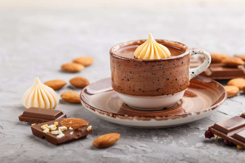 Cup of hot chocolate and pieces of milk chocolate with almonds on a gray concrete background