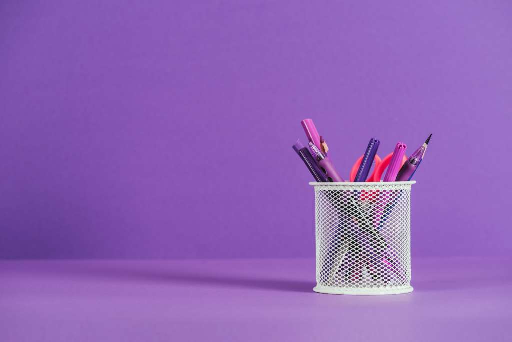 pen holder with various pens and pencils on purple surface