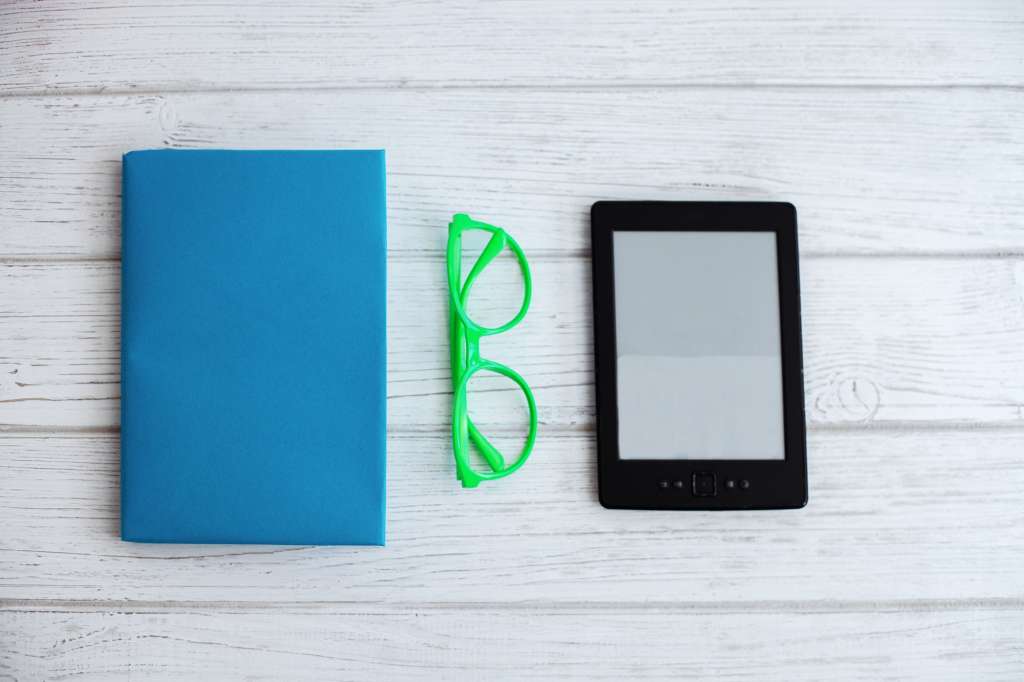 Printed books and e-book on a white background and glasses.
