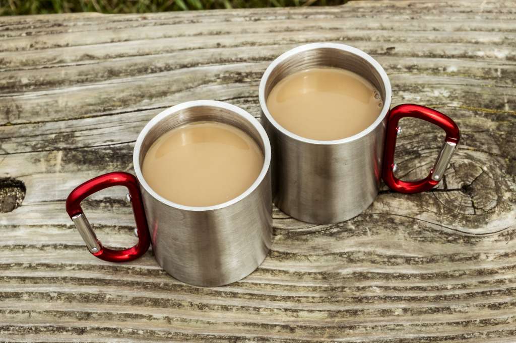 Two metal camping mugs of tea on a wooden table.