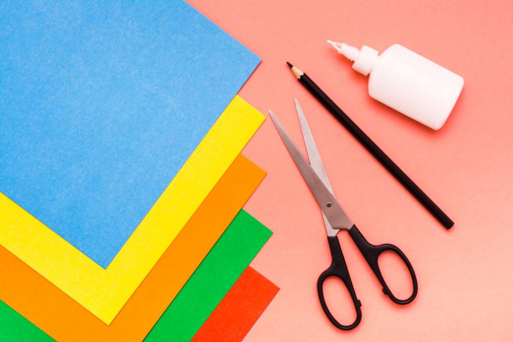 Items for creativity - sheets of colored cardboard, scissors, pencil and glue on a red background