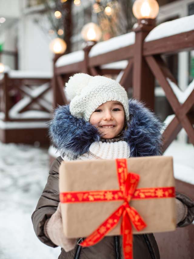 Portrait of joyful girl with a gift box for Christmas on a city street in winter