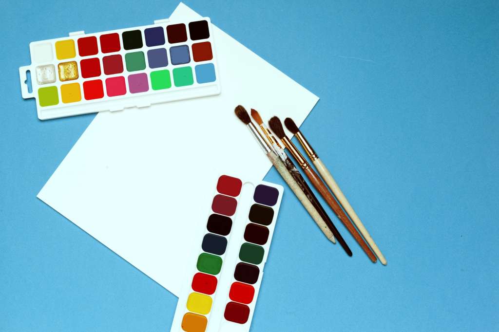 Art supplies. Watercolor paints and brushes on bright blue background