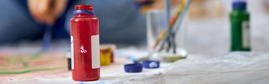 Close up shot of red acrylic paint in jar. Woman working on painting in the