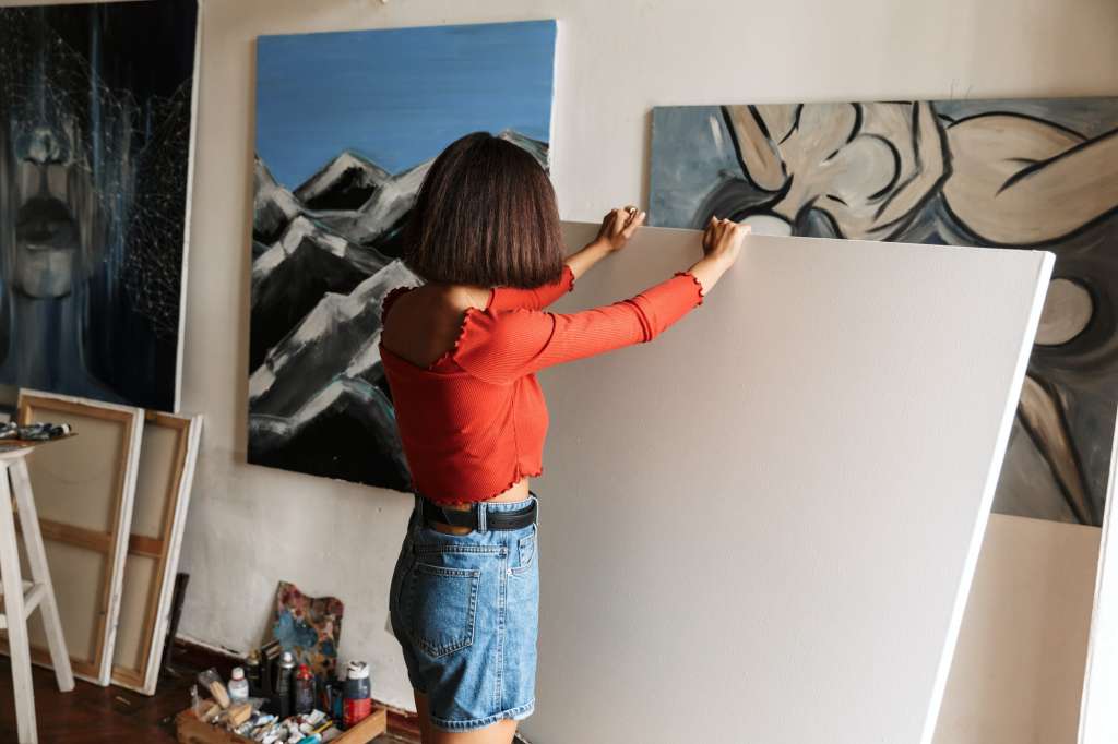Portrait of woman holding blanc paint canvas while drawing in studio